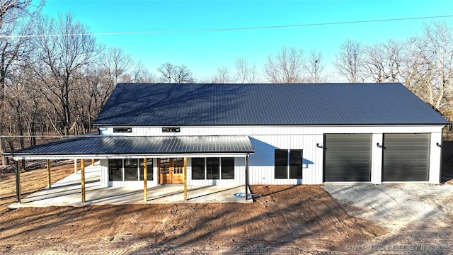 rear view of property featuring driveway, covered porch, and metal roof