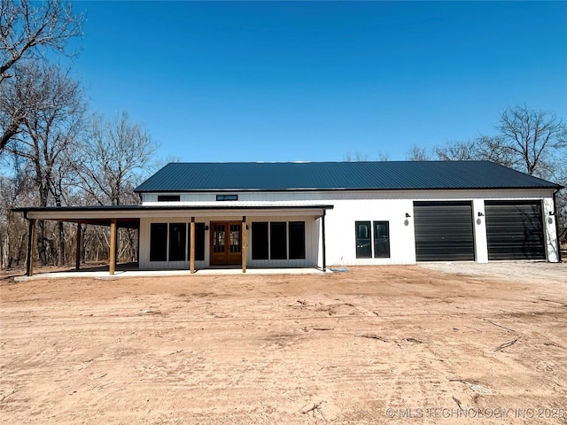 back of property featuring french doors, a garage, dirt driveway, and metal roof