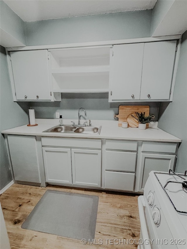 kitchen with white cabinetry, white gas stove, sink, and light hardwood / wood-style flooring