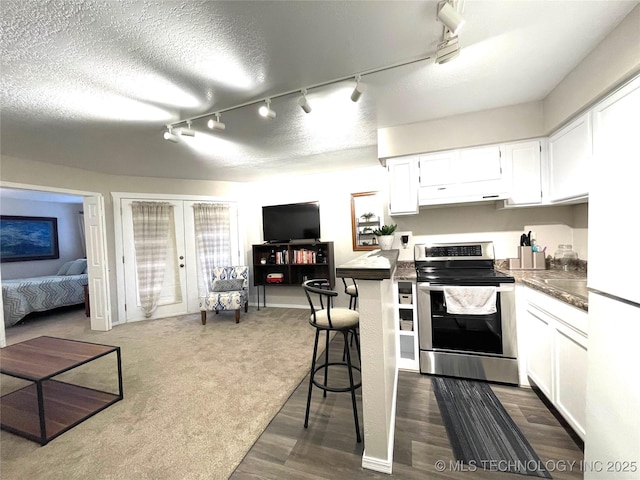 kitchen with white cabinets, dark countertops, track lighting, stainless steel range with electric stovetop, and under cabinet range hood