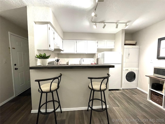 kitchen with dark countertops, stacked washing maching and dryer, freestanding refrigerator, stainless steel microwave, and under cabinet range hood