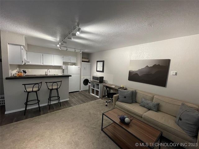 6663 S Victor Ave Unit H # 305, Tulsa, OK 74136 - living area with stacked washer and clothes dryer, a textured ceiling, dark wood finished floors, track lighting, and dark colored carpet