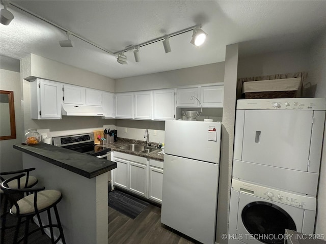 6663 S Victor Ave Unit H # 305, Tulsa, OK 74136 - kitchen featuring freestanding refrigerator, under cabinet range hood, stacked washer and clothes dryer, dark countertops, and rail lighting