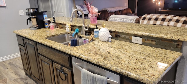 kitchen with stainless steel dishwasher, light stone countertops, sink, and light wood-type flooring