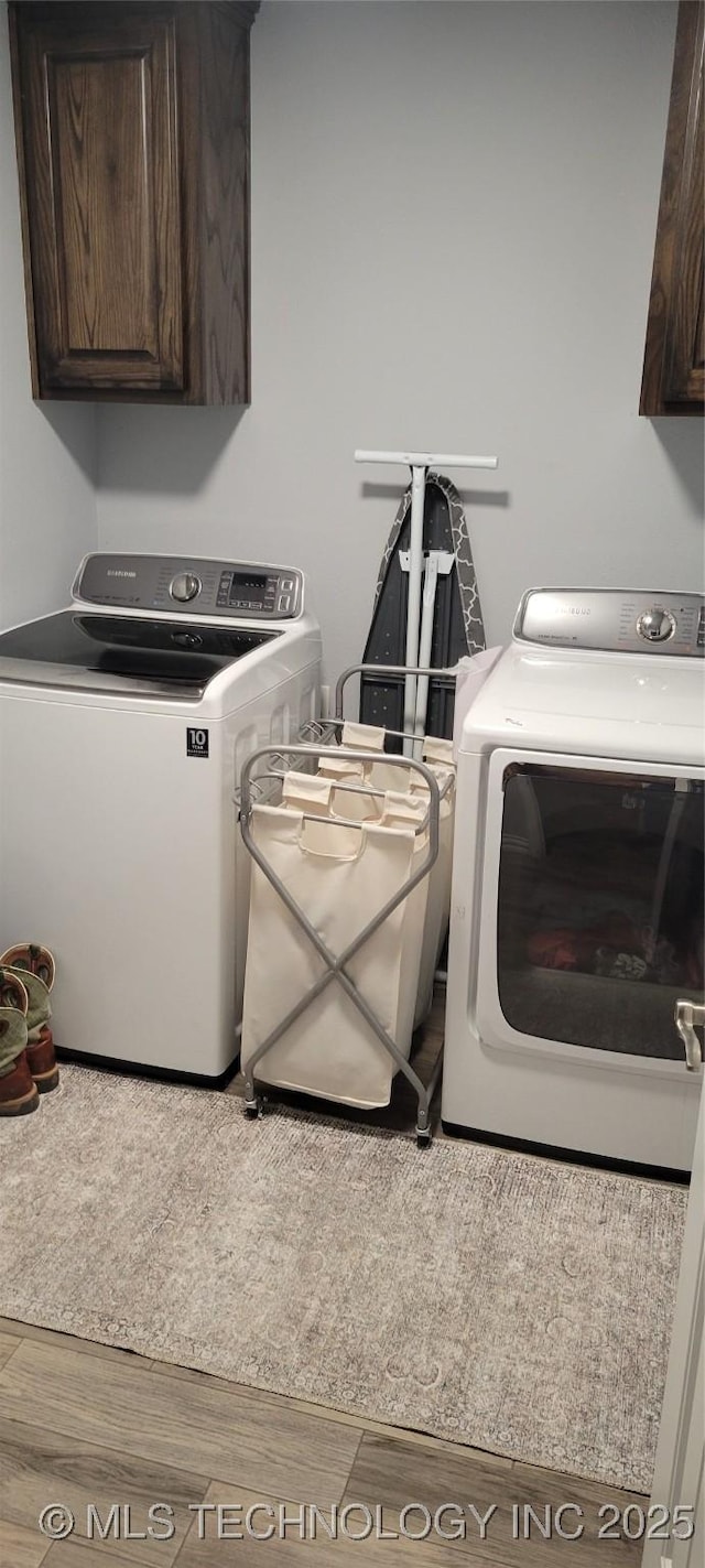 laundry area featuring washer and dryer, wood-type flooring, and cabinets