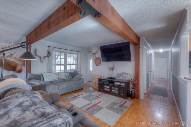 living room with beamed ceiling, a textured ceiling, and wood finished floors