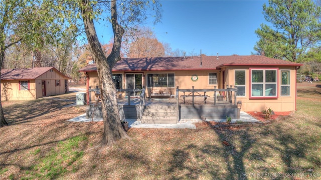 back of property with an outbuilding, a storage shed, a yard, a wooden deck, and stucco siding