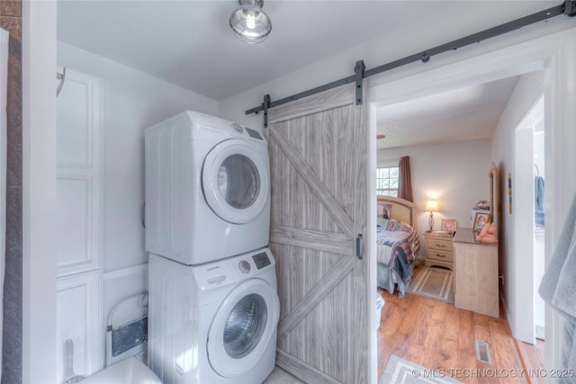 laundry room with stacked washer and dryer, a barn door, laundry area, visible vents, and light wood finished floors