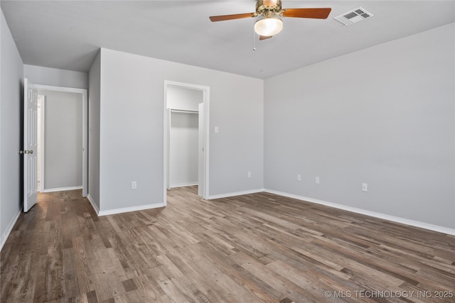 unfurnished bedroom featuring ceiling fan, a walk in closet, hardwood / wood-style floors, and a closet