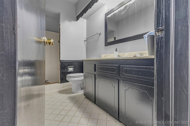 bathroom with tile patterned flooring, vanity, toilet, and tiled shower