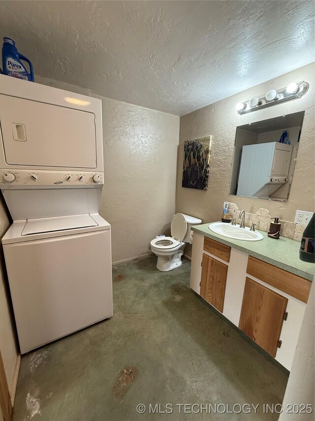 half bathroom featuring vanity, stacked washing maching and dryer, a textured ceiling, toilet, and a textured wall
