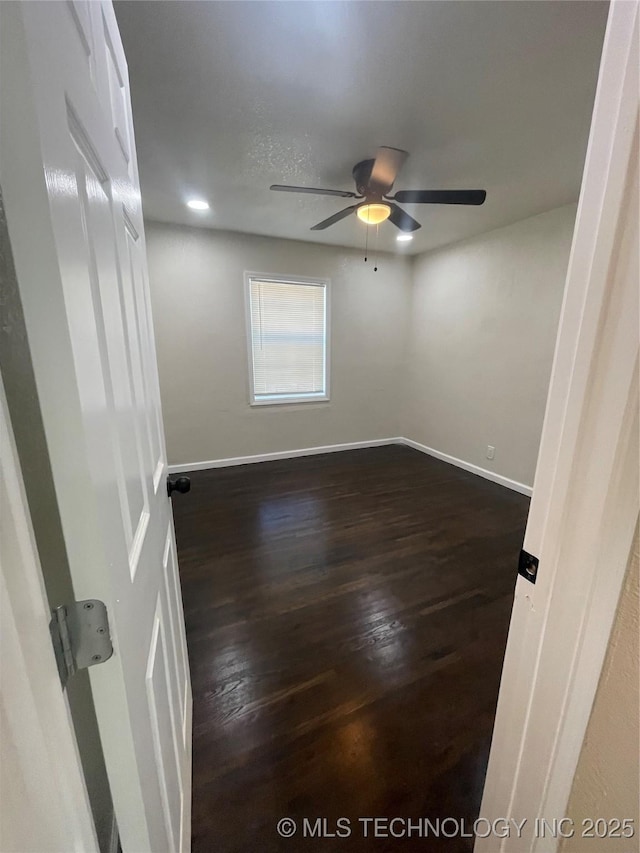 empty room with dark wood finished floors, a ceiling fan, and baseboards