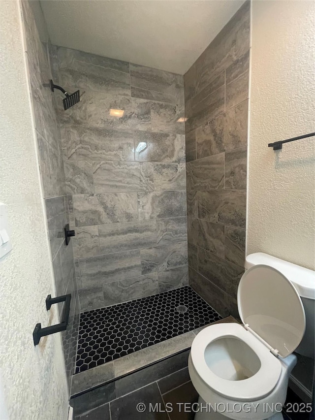 bathroom with a textured wall, a shower stall, and toilet