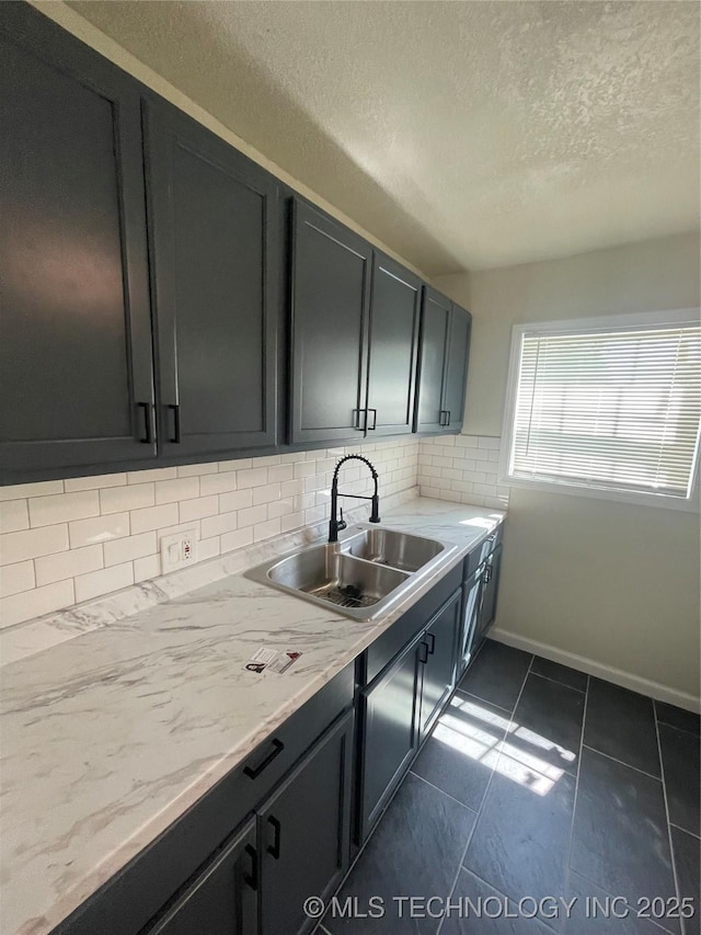 kitchen featuring tasteful backsplash, baseboards, light stone counters, dark cabinets, and a sink