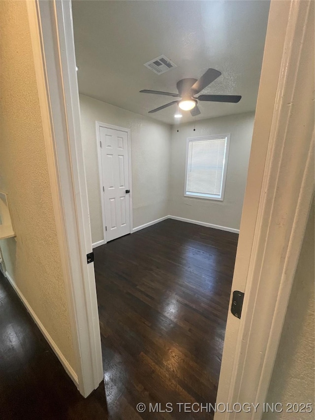 empty room featuring ceiling fan, dark wood-style flooring, visible vents, and baseboards