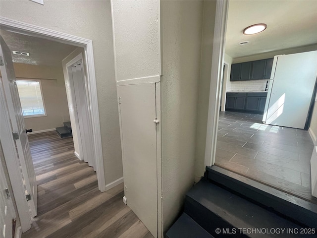 hallway featuring dark wood-type flooring, visible vents, a textured wall, and baseboards