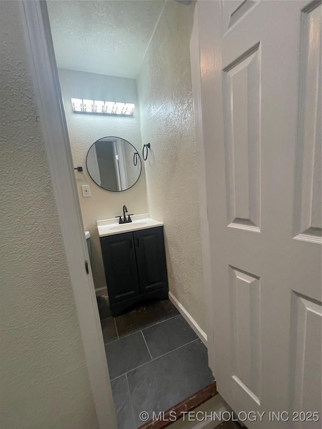 half bath featuring baseboards, a textured wall, tile patterned flooring, a textured ceiling, and vanity