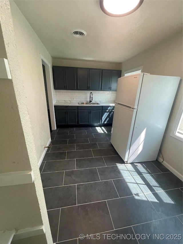 kitchen with light countertops, visible vents, backsplash, freestanding refrigerator, and a sink