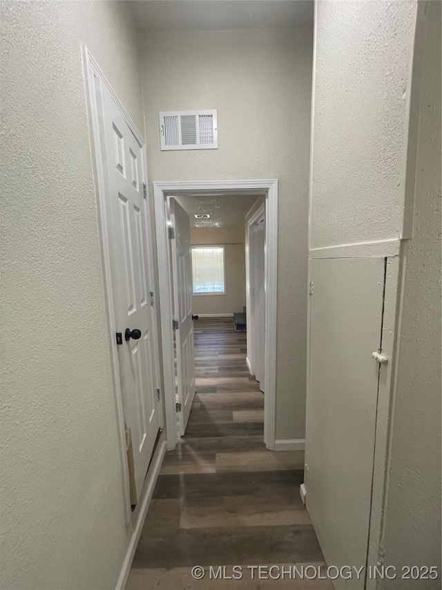 corridor featuring dark wood-type flooring, visible vents, and baseboards