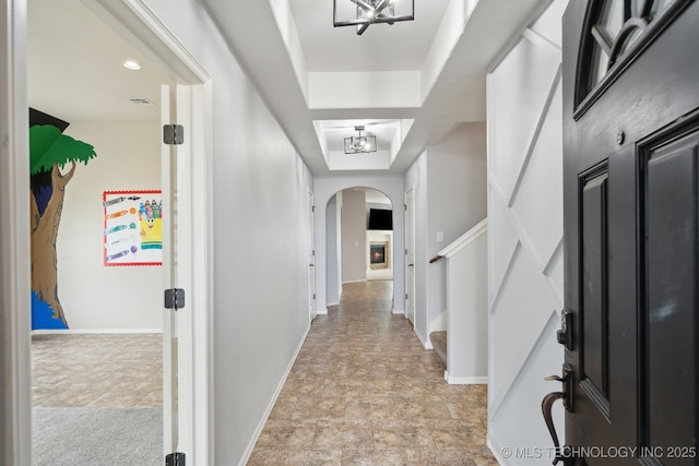 corridor with a raised ceiling and an inviting chandelier