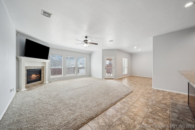 unfurnished living room featuring a tile fireplace, light colored carpet, and ceiling fan