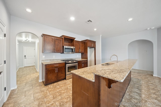 kitchen featuring appliances with stainless steel finishes, a breakfast bar, sink, light stone countertops, and a kitchen island with sink