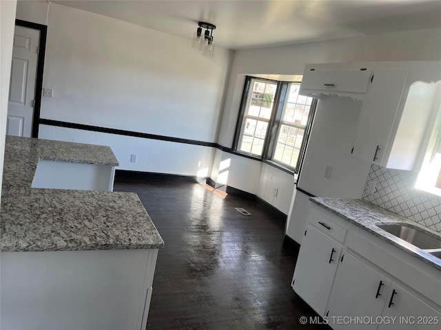 kitchen with sink, light stone counters, dark hardwood / wood-style floors, white cabinets, and backsplash