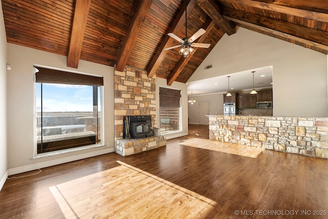 unfurnished living room featuring beamed ceiling, a wood stove, dark hardwood / wood-style flooring, ceiling fan, and wood ceiling