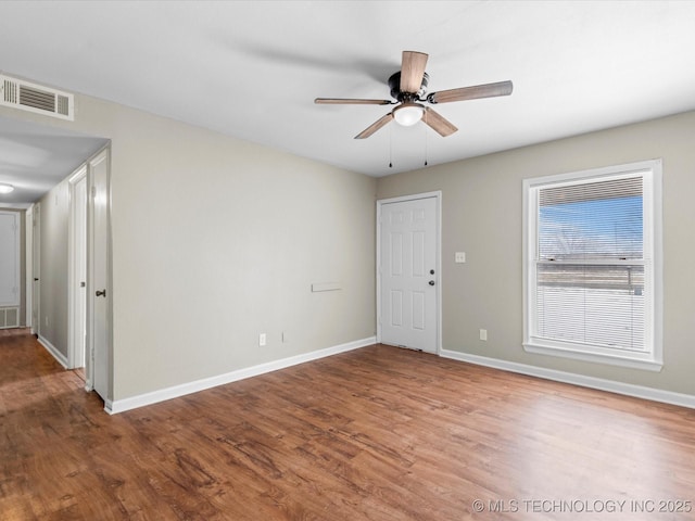 empty room with visible vents, a ceiling fan, baseboards, and wood finished floors