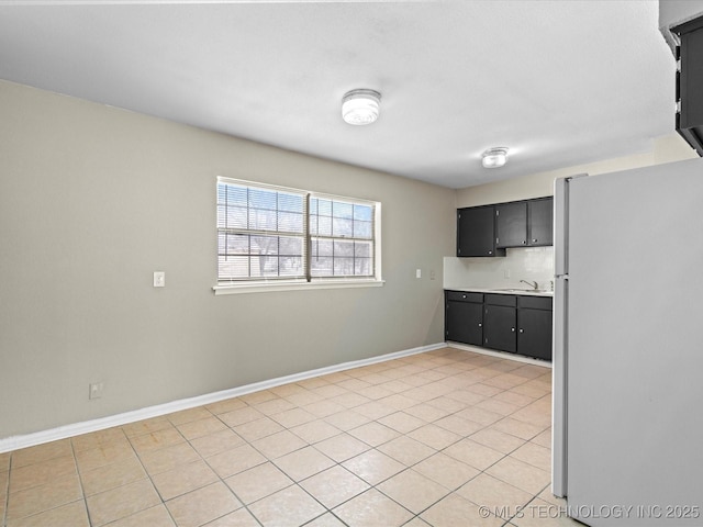 kitchen featuring baseboards, freestanding refrigerator, a sink, light countertops, and dark cabinets