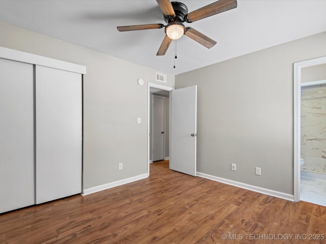 unfurnished bedroom featuring visible vents, ensuite bath, wood finished floors, a closet, and baseboards