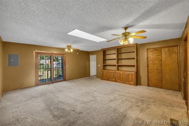 unfurnished living room featuring light carpet, a skylight, electric panel, and ceiling fan