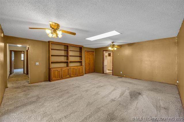 interior space featuring ceiling fan, light colored carpet, a skylight, and a textured ceiling