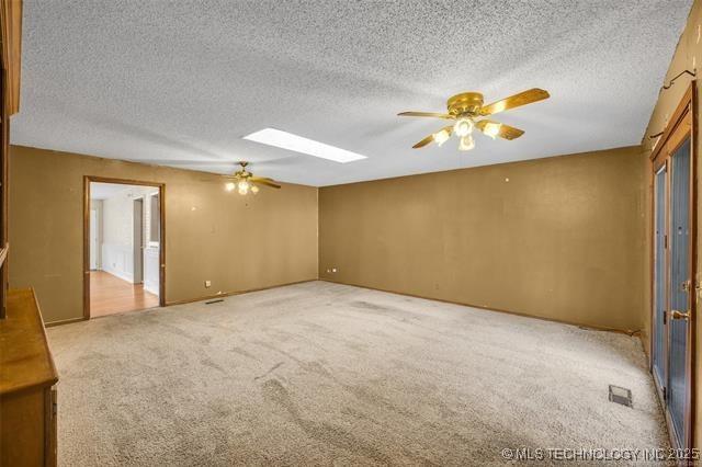 spare room with ceiling fan, a skylight, light carpet, and a textured ceiling