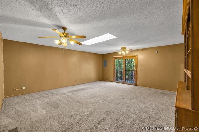 empty room featuring ceiling fan, carpet flooring, a skylight, and a textured ceiling