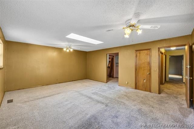 carpeted empty room with a textured ceiling, ceiling fan, and a skylight