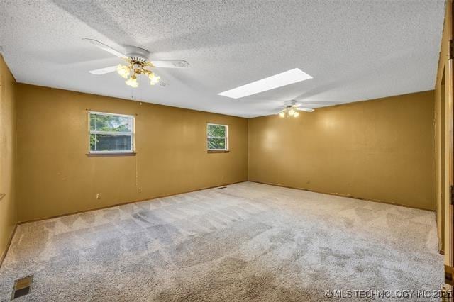 carpeted spare room with ceiling fan, a skylight, and a textured ceiling