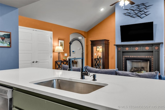 kitchen featuring a fireplace, lofted ceiling, sink, stainless steel dishwasher, and ceiling fan