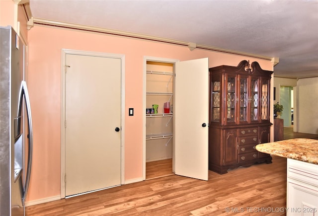 kitchen with stainless steel refrigerator with ice dispenser, crown molding, and light wood-type flooring