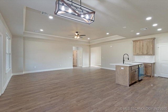 kitchen with a raised ceiling, ceiling fan, hardwood / wood-style flooring, and a center island with sink