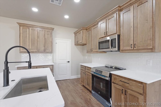 kitchen featuring sink, backsplash, appliances with stainless steel finishes, and light hardwood / wood-style floors