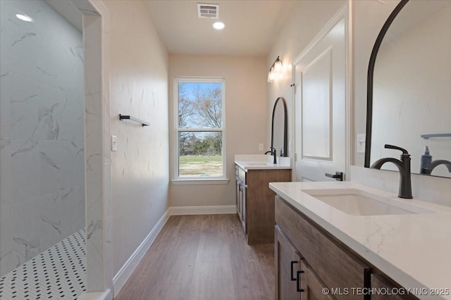 bathroom with hardwood / wood-style flooring, a tile shower, and vanity