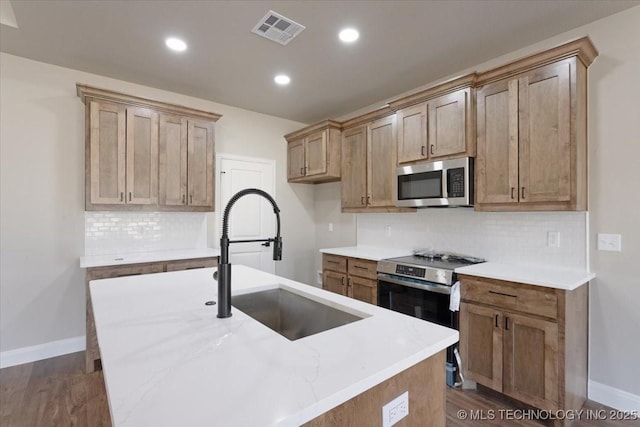 kitchen with a center island with sink, appliances with stainless steel finishes, sink, and tasteful backsplash