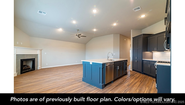 kitchen with vaulted ceiling, appliances with stainless steel finishes, a fireplace, an island with sink, and hardwood / wood-style flooring