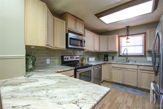 kitchen with sink, light brown cabinets, appliances with stainless steel finishes, kitchen peninsula, and light hardwood / wood-style floors