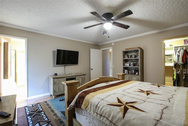 bedroom featuring a walk in closet, a textured ceiling, ornamental molding, ceiling fan, and light hardwood / wood-style floors