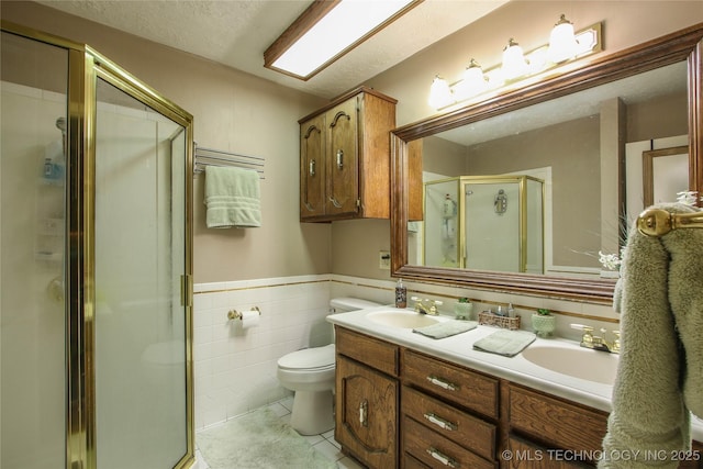 bathroom with tile walls, vanity, a shower with shower door, tile patterned floors, and toilet