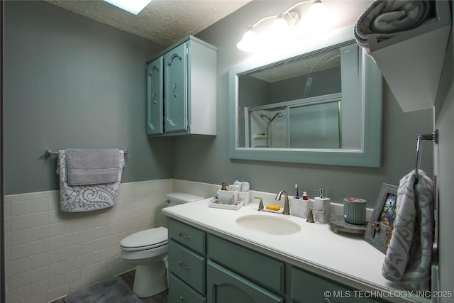 bathroom with a shower with shower door, tile walls, vanity, toilet, and a textured ceiling