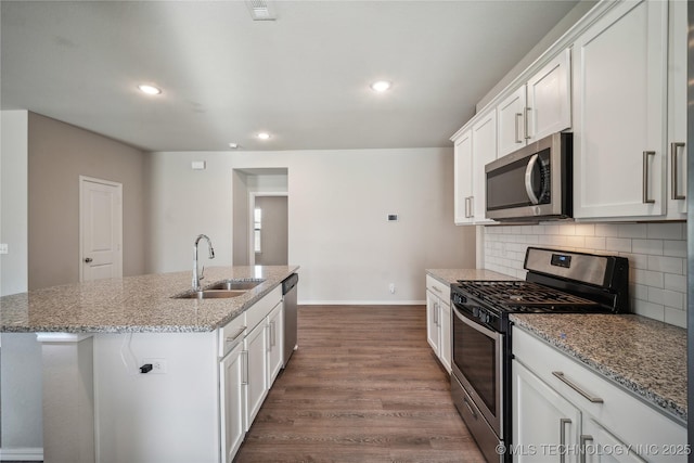 kitchen with sink, a kitchen island with sink, white cabinetry, stainless steel appliances, and light stone counters