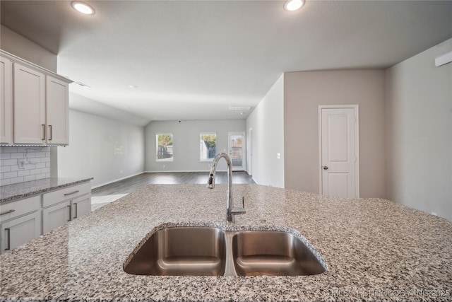 kitchen with light stone counters, wood-type flooring, sink, and backsplash